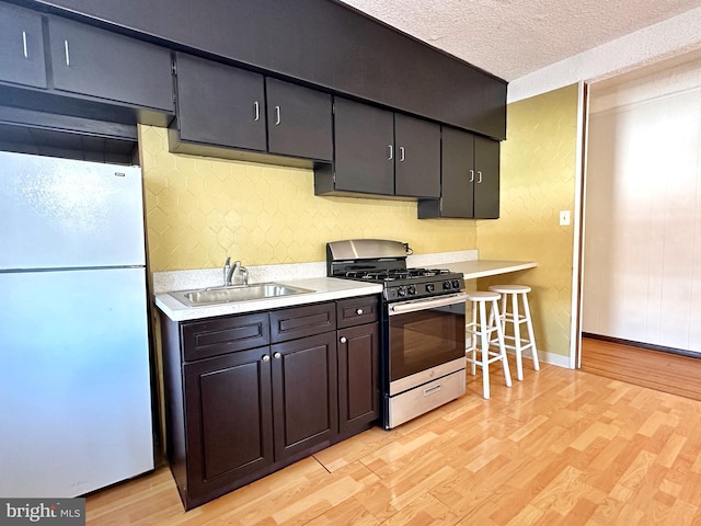 kitchen with stainless steel range with gas cooktop, sink, light wood-type flooring, a textured ceiling, and white refrigerator