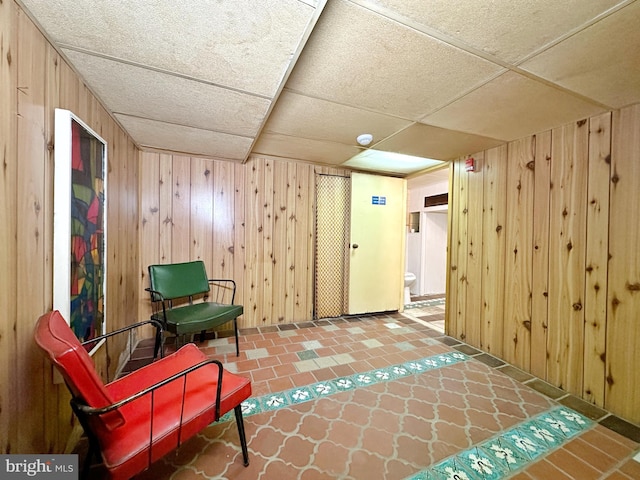 sitting room featuring wooden walls, tile flooring, and a drop ceiling