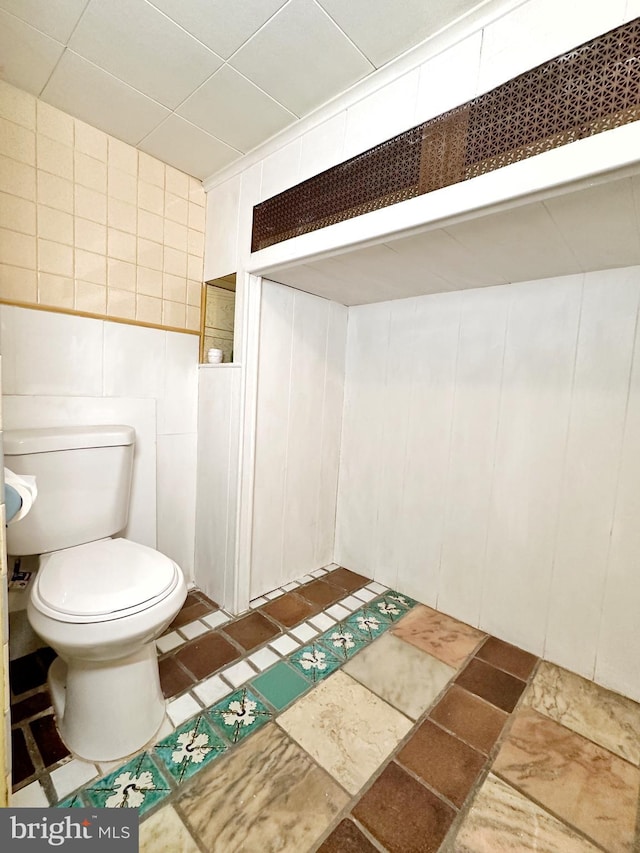 bathroom with toilet, tile flooring, and tile walls