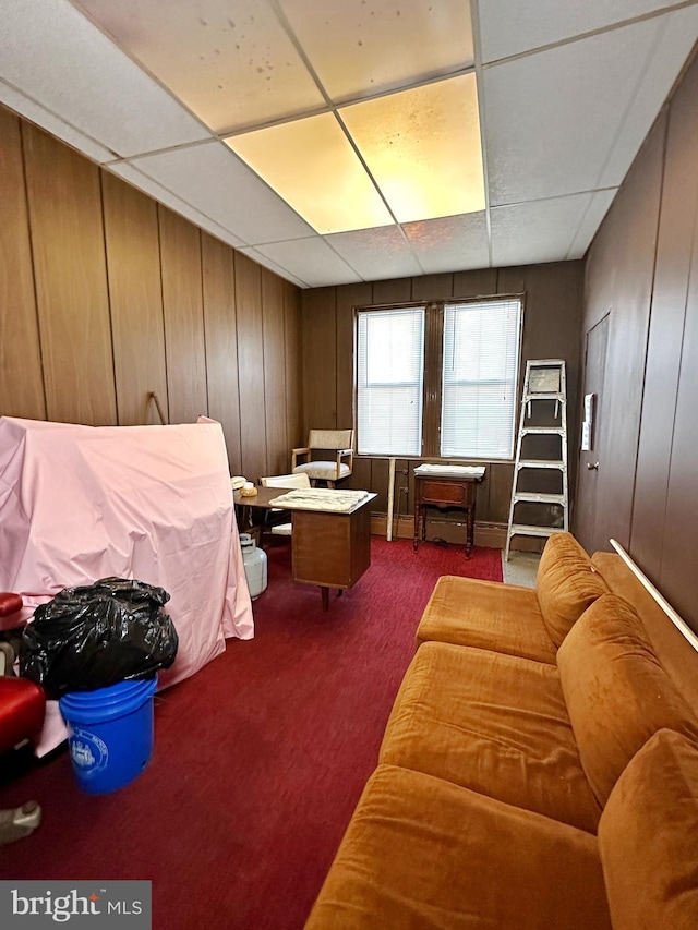 interior space with carpet floors, wooden walls, and a drop ceiling