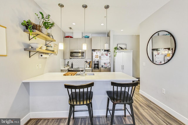 kitchen with backsplash, kitchen peninsula, appliances with stainless steel finishes, sink, and hardwood / wood-style flooring