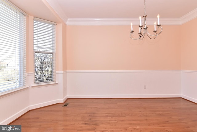 unfurnished room with ornamental molding, light wood-type flooring, plenty of natural light, and a chandelier