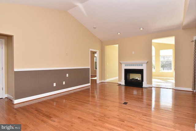 unfurnished living room with light hardwood / wood-style floors, high vaulted ceiling, and a multi sided fireplace