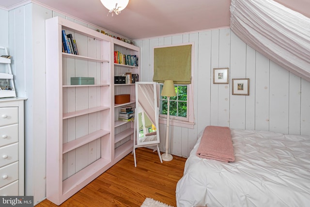 bedroom with wood walls, vaulted ceiling, and light hardwood / wood-style floors