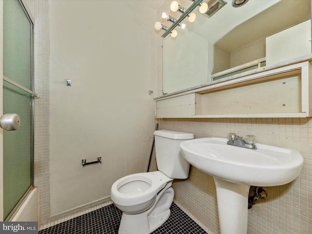 bathroom with tile patterned flooring, toilet, bath / shower combo with glass door, and tile walls