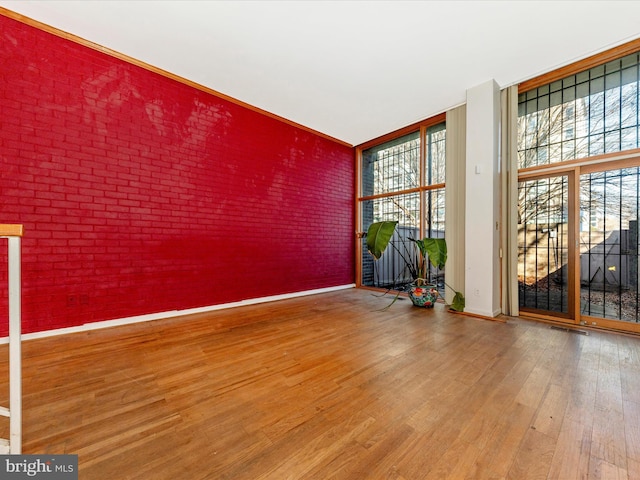 spare room with hardwood / wood-style flooring, a wealth of natural light, and brick wall