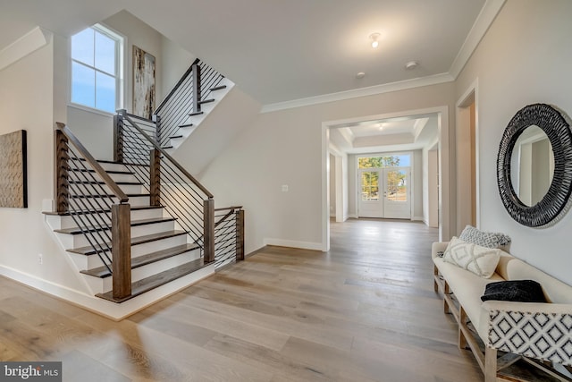 foyer featuring a raised ceiling, crown molding, french doors, and light wood-type flooring