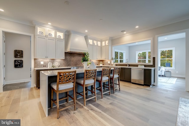 kitchen with a kitchen island, stainless steel dishwasher, white cabinetry, custom range hood, and light wood-type flooring