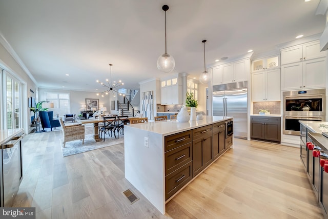 kitchen featuring tasteful backsplash, white cabinets, built in appliances, a notable chandelier, and hanging light fixtures