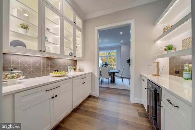 bar with backsplash, light hardwood / wood-style floors, white cabinets, beverage cooler, and crown molding