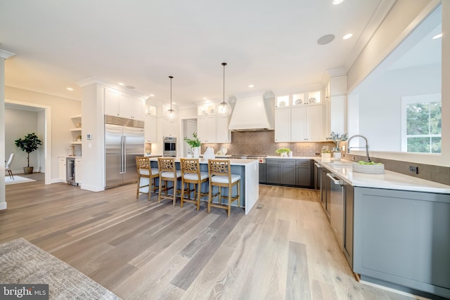 kitchen with custom exhaust hood, light hardwood / wood-style flooring, stainless steel appliances, and white cabinetry