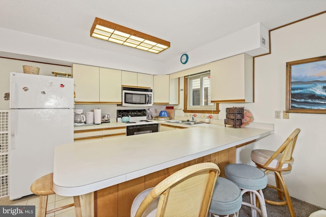 kitchen with cream cabinets, a breakfast bar, sink, white appliances, and kitchen peninsula