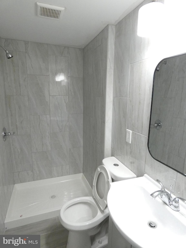 bathroom featuring sink, tiled shower, tile walls, and toilet