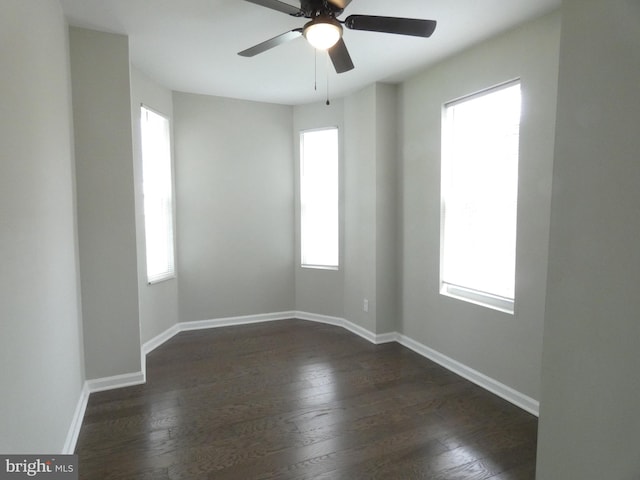 empty room with a healthy amount of sunlight, dark wood-type flooring, and ceiling fan