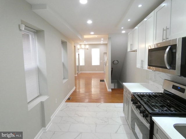 kitchen with appliances with stainless steel finishes, a chandelier, light tile floors, and white cabinetry