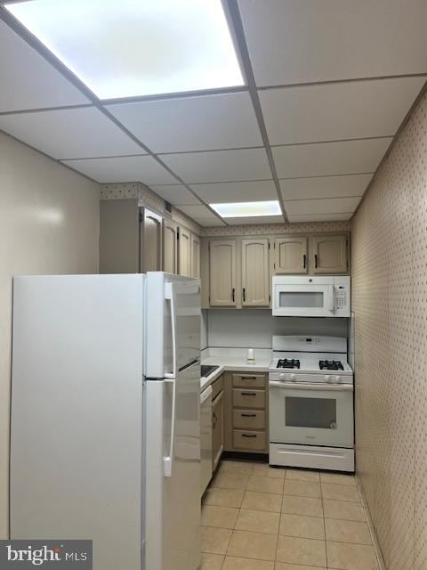 kitchen with a paneled ceiling, white appliances, and light tile flooring