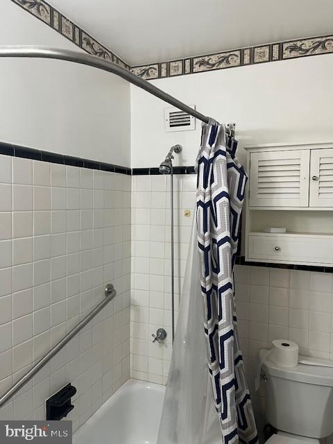 bathroom with toilet, shower / bath combo with shower curtain, and tile walls