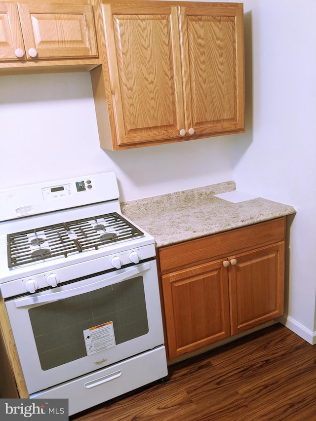 kitchen with dark wood-type flooring, light stone countertops, and white range with gas stovetop