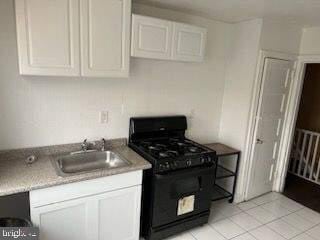 kitchen featuring white cabinets, black range with gas stovetop, light tile patterned floors, and sink