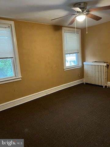 unfurnished room with carpet, radiator, a wealth of natural light, and ceiling fan