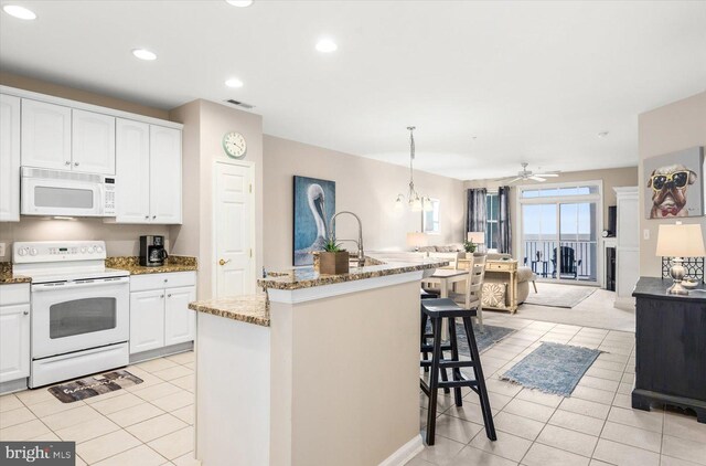 kitchen with white appliances, pendant lighting, a center island with sink, ceiling fan with notable chandelier, and white cabinetry