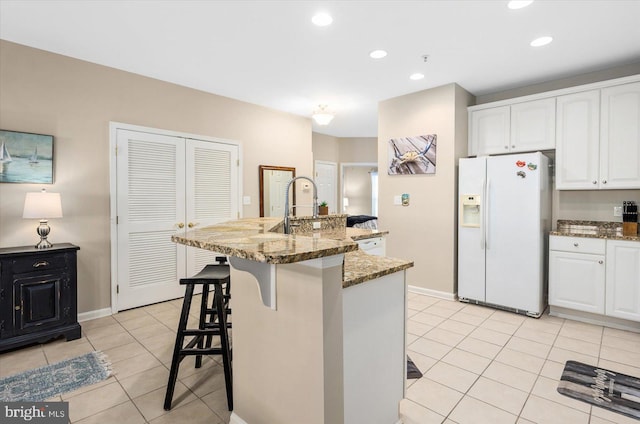 kitchen featuring white cabinets, white fridge with ice dispenser, a breakfast bar, and dark stone countertops