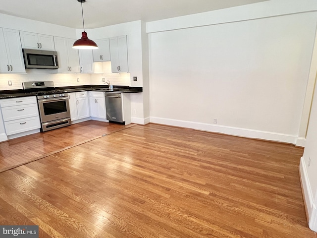 kitchen with appliances with stainless steel finishes, backsplash, sink, decorative light fixtures, and white cabinetry