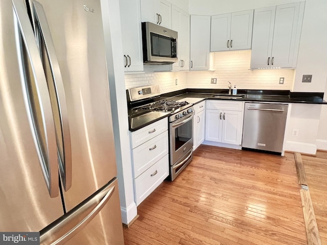 kitchen featuring sink, light hardwood / wood-style flooring, decorative backsplash, white cabinets, and appliances with stainless steel finishes