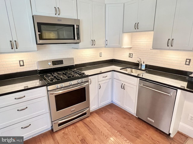 kitchen featuring sink, stainless steel appliances, tasteful backsplash, white cabinets, and light wood-type flooring