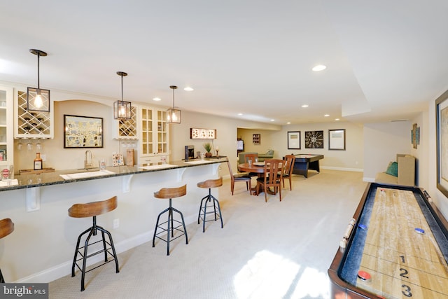 kitchen featuring a breakfast bar area, light colored carpet, pendant lighting, and dark stone counters