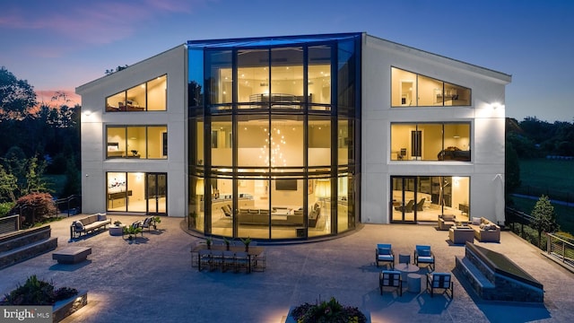 back house at dusk with outdoor lounge area and a patio area