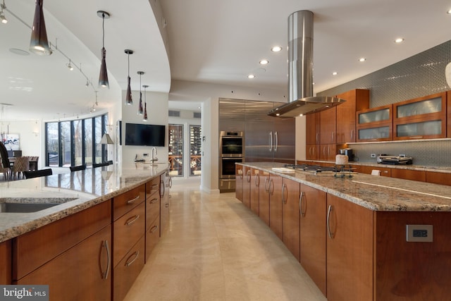 kitchen featuring a kitchen island, light stone counters, stainless steel appliances, decorative light fixtures, and island exhaust hood