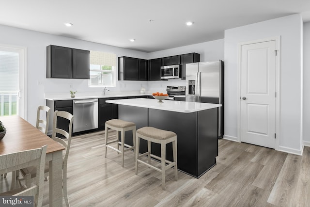 kitchen with light hardwood / wood-style flooring, a kitchen bar, a center island, sink, and appliances with stainless steel finishes