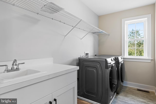 laundry area featuring separate washer and dryer, sink, washer hookup, light wood-type flooring, and cabinets