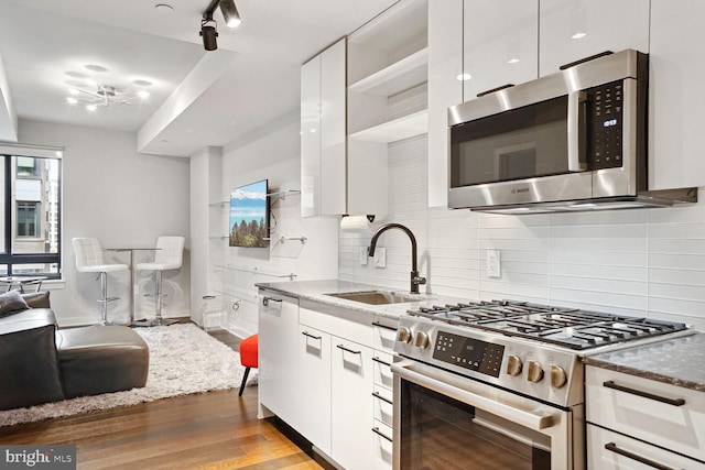 kitchen with stainless steel appliances, white cabinets, sink, light hardwood / wood-style floors, and backsplash