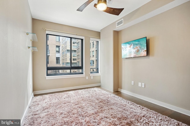 empty room with dark wood-type flooring, ceiling fan, and a wealth of natural light