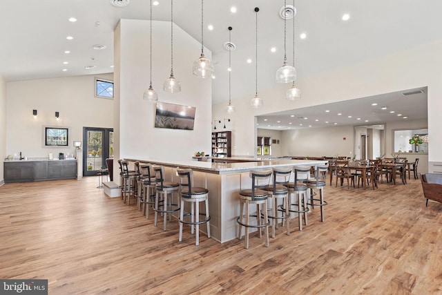 kitchen featuring pendant lighting, a breakfast bar area, high vaulted ceiling, light hardwood / wood-style flooring, and light stone countertops