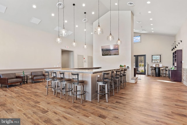 kitchen featuring decorative light fixtures, a kitchen bar, high vaulted ceiling, light hardwood / wood-style flooring, and a kitchen island