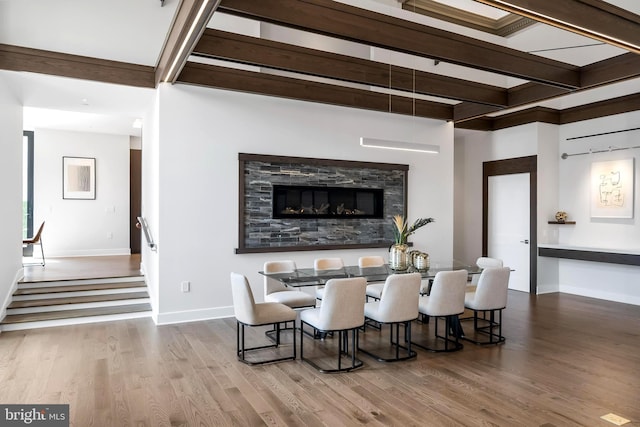 dining room featuring wood-type flooring, beam ceiling, and a stone fireplace