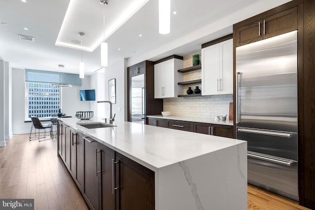 kitchen with pendant lighting, light wood-type flooring, backsplash, stainless steel built in fridge, and white cabinets