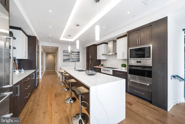 kitchen featuring pendant lighting, light wood-type flooring, tasteful backsplash, and wall chimney exhaust hood