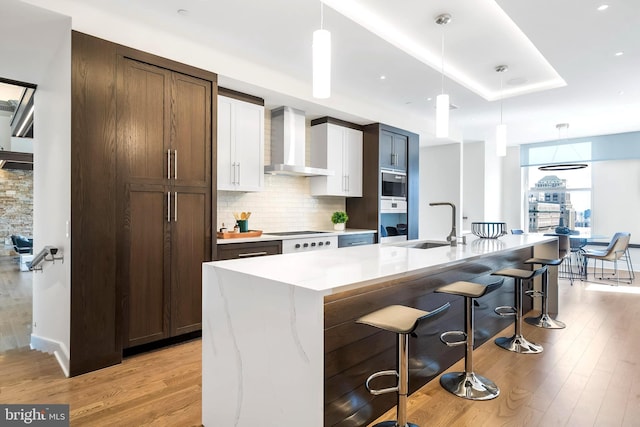 kitchen with hanging light fixtures, backsplash, light wood-type flooring, and wall chimney range hood