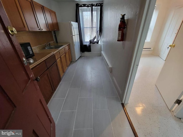 kitchen featuring light tile floors, a baseboard heating unit, sink, and white refrigerator