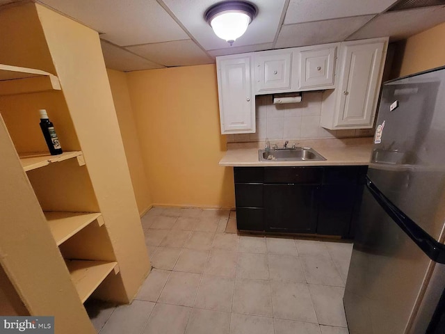 kitchen with white cabinets, stainless steel refrigerator, a drop ceiling, and sink