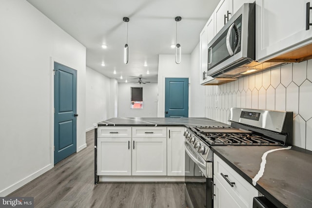 kitchen with dark countertops, white cabinetry, appliances with stainless steel finishes, a peninsula, and decorative backsplash