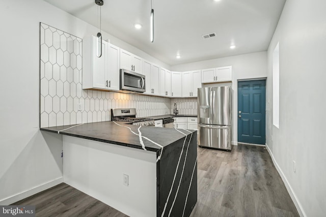 kitchen featuring visible vents, a peninsula, stainless steel appliances, decorative backsplash, and dark countertops