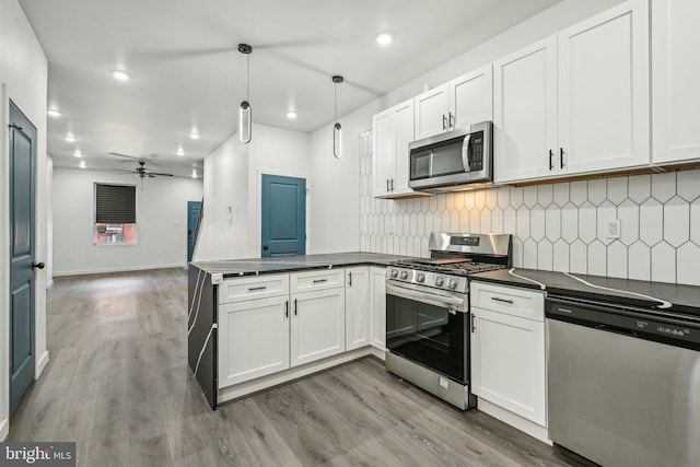 kitchen with dark countertops, light wood finished floors, appliances with stainless steel finishes, and a peninsula