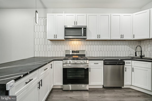 kitchen with dark wood-style floors, a sink, stainless steel appliances, dark countertops, and tasteful backsplash