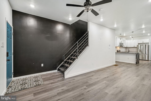 unfurnished living room featuring baseboards, ceiling fan, stairs, and light wood finished floors