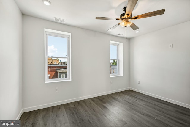 spare room featuring visible vents, baseboards, a ceiling fan, and dark wood-style flooring